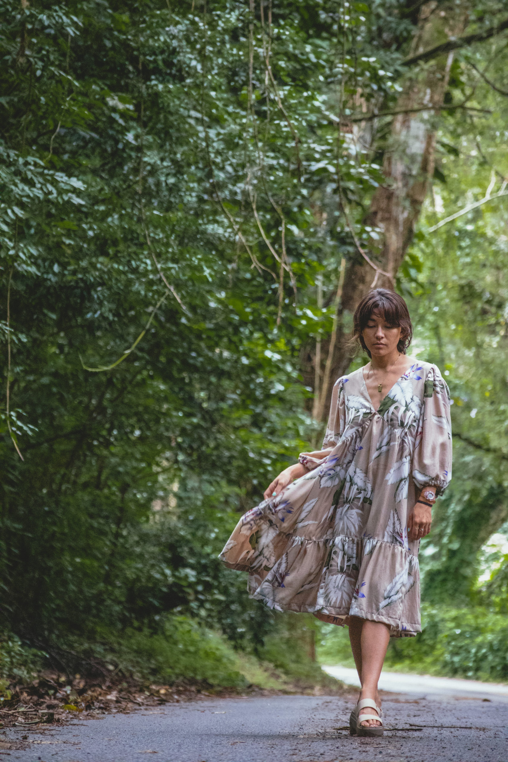 Woman in a beige tropical patterned dress walks on a forested road